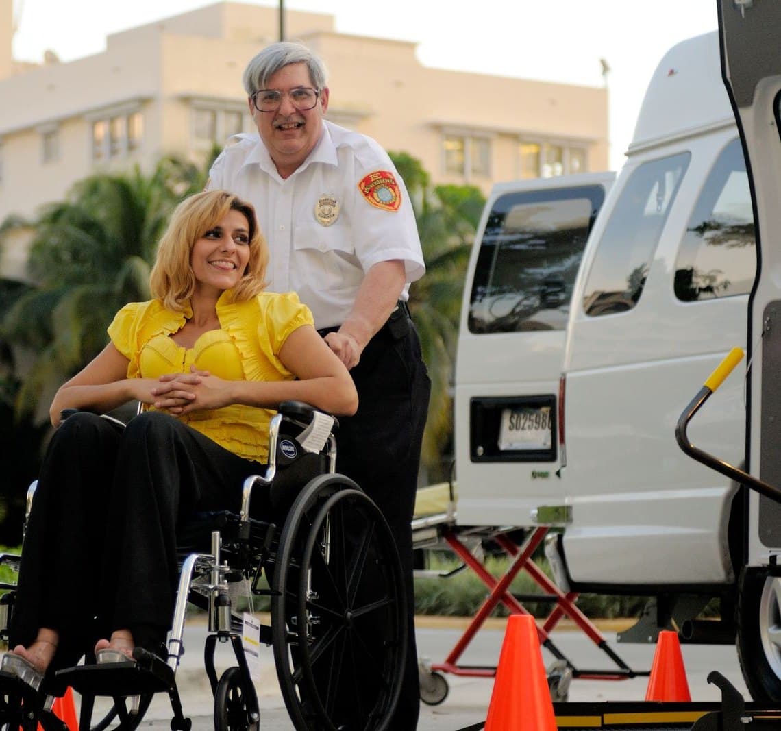 A driver walking a passenger in a wheelchair toward an accessible van.
