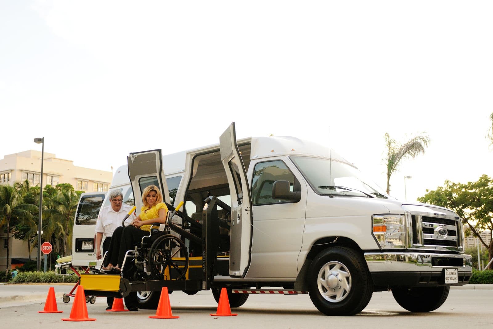 A driver assisting a passenger in a wheelchair onto the lift of an accessible van.