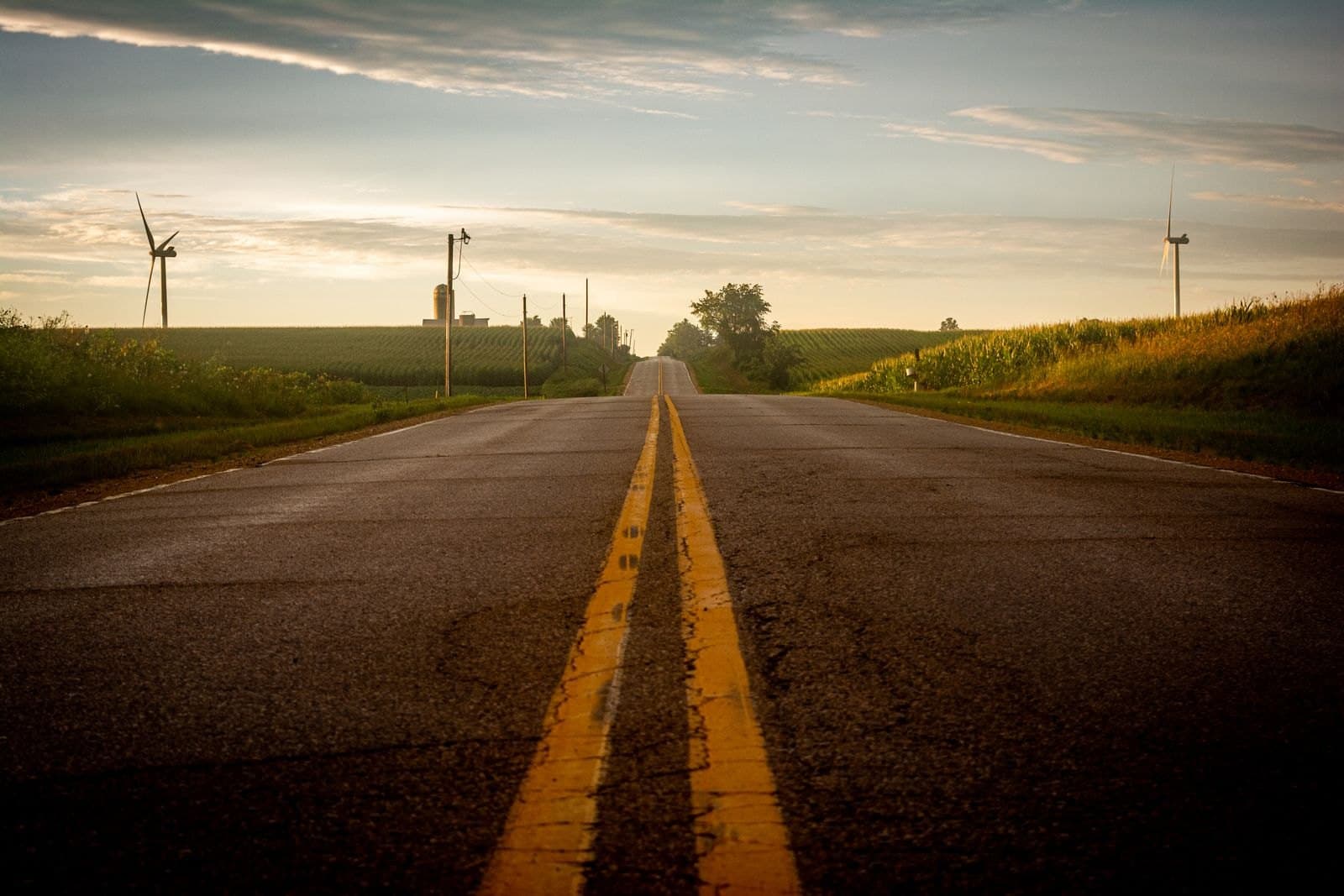 A two-lane road running between corn fields under a wide Midwest sky.